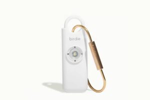 A sleek white personal safety device with a circular alarm button and a gold keyring attachment, branded birdie.