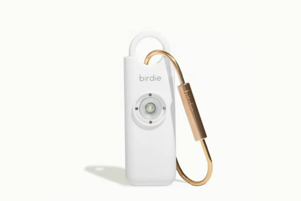 A sleek white personal safety device with a circular alarm button and a gold keyring attachment, branded birdie.