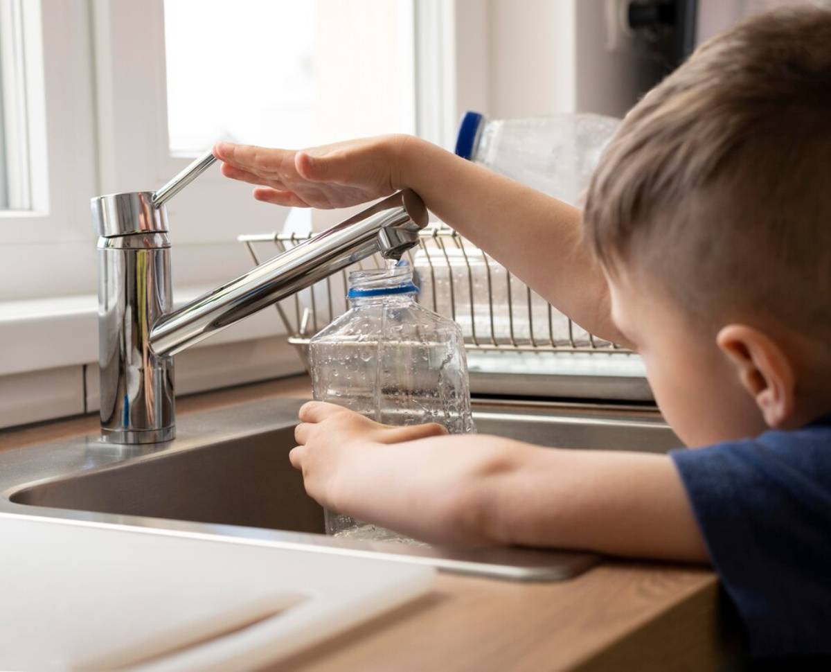 A young boy fills a plastic water bottle from a modern kitchen faucet, capturing the moment of learning and exploration.