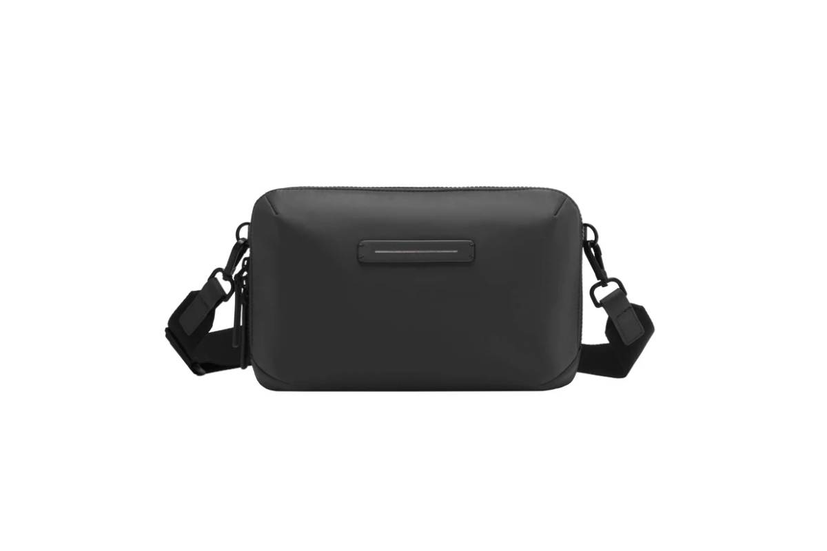 A sleek, black crossbody bag with a zip closure and adjustable strap, featuring minimalist design and a simple logo. 