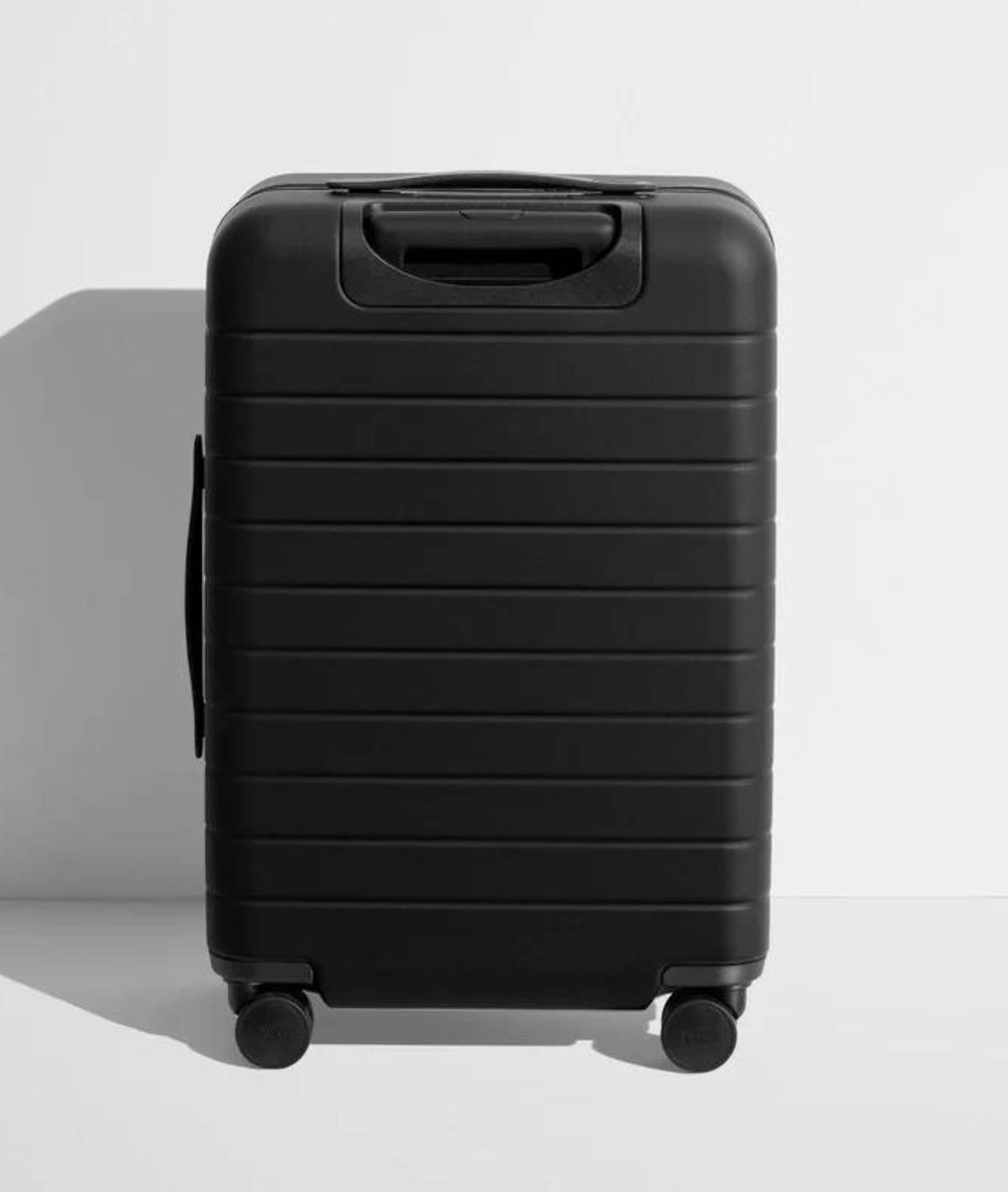  A sleek, black hard-shell suitcase with textured stripes, featuring a top handle and wheels for easy mobility against a minimal background.