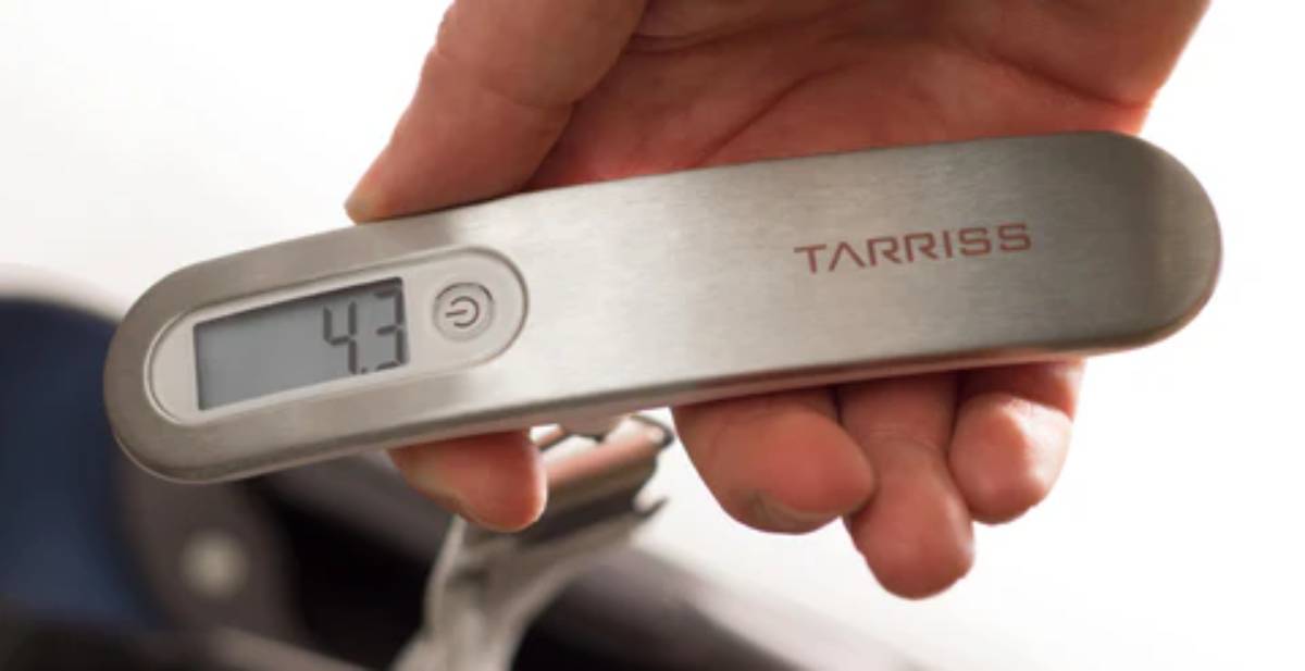 A hand holds a silver digital luggage scale showing a weight of 4.3 kg, marked with the brand name TARRISS. 