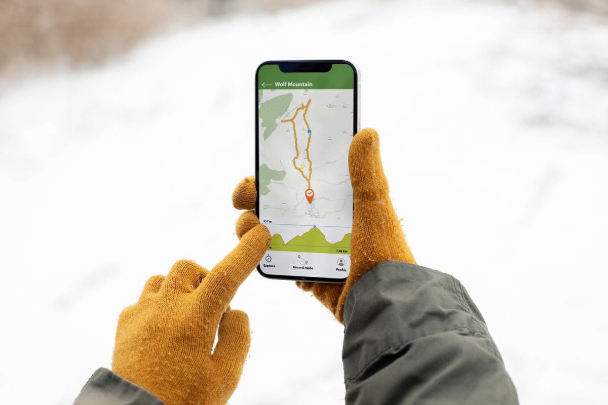  A person in orange gloves points at a smartphone displaying a snowy route map to Wolf Mountain.