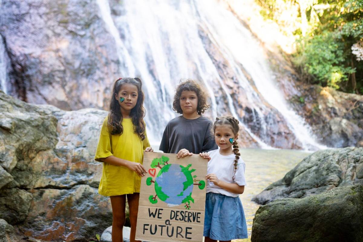Three children stand by a waterfall holding a sign that reads We Deserve a Future adorned with a drawing of the Earth. 