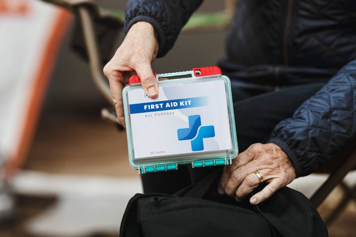 A person holds an all-purpose first aid kit labeled FIRST AID KIT while reaching into a black bag. 