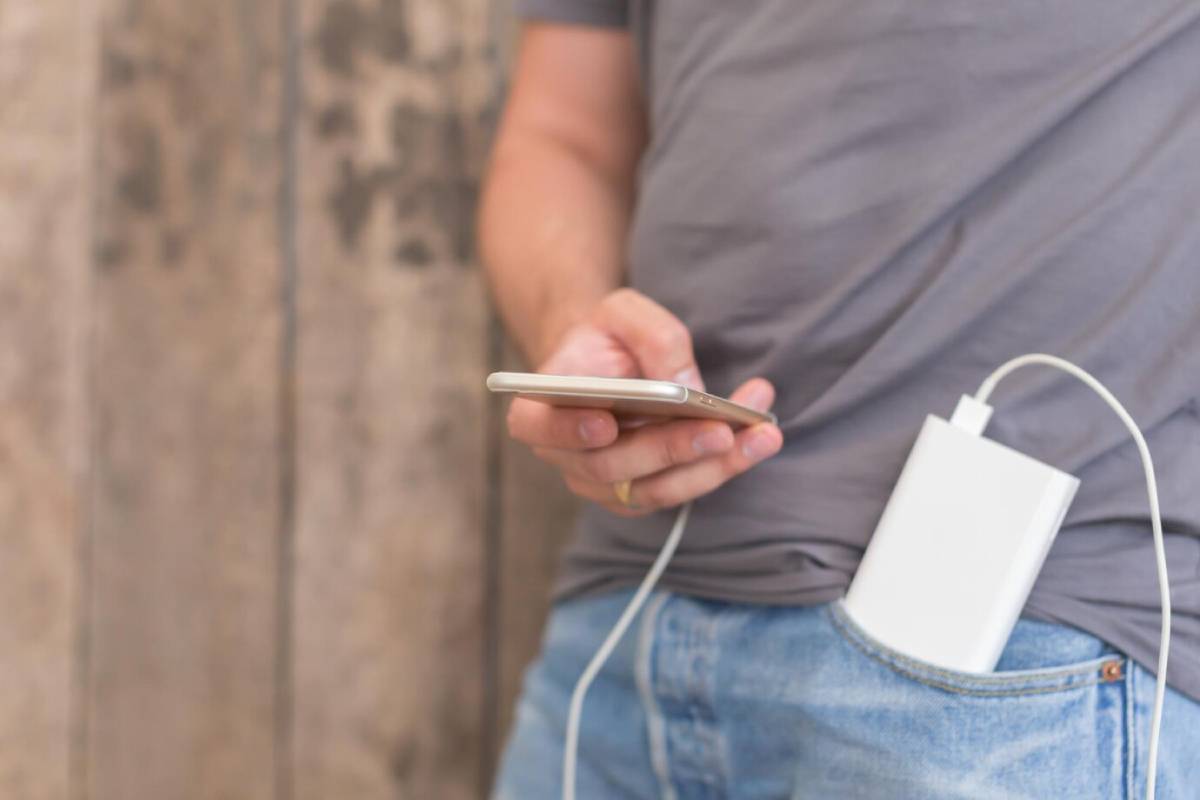  A person in a gray shirt uses a smartphone while a power bank is plugged into it, resting in a denim pocket.