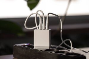 A close-up of a small white power hub with multiple cables plugged in, sitting on a black power strip against a blurred background.